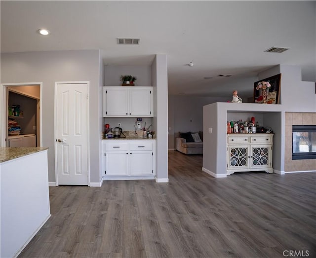 interior space with light stone counters, light wood-type flooring, white cabinetry, washer and clothes dryer, and a tiled fireplace