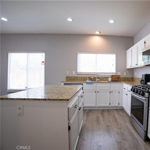 kitchen with stainless steel appliances, white cabinetry, light stone countertops, and a healthy amount of sunlight