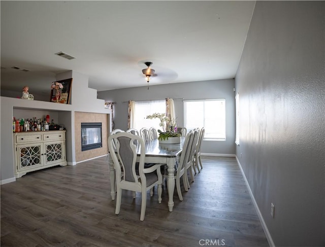 dining room featuring ceiling fan, dark wood-type flooring, and a fireplace