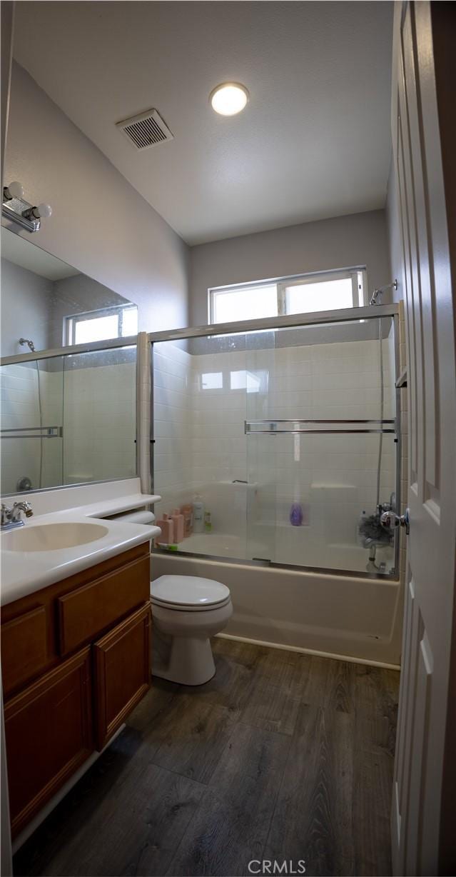 full bathroom featuring hardwood / wood-style flooring, shower / bath combination with glass door, vanity, and toilet