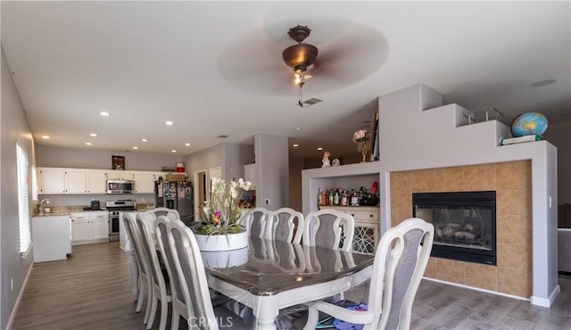 dining area featuring ceiling fan, sink, dark wood-type flooring, and a tile fireplace