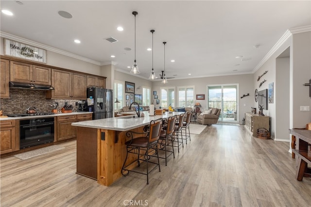 kitchen with tasteful backsplash, visible vents, open floor plan, under cabinet range hood, and black appliances