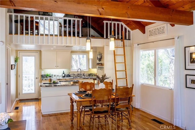 dining space with wood ceiling, light hardwood / wood-style floors, sink, and vaulted ceiling with beams