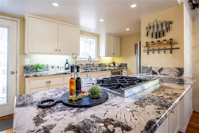 kitchen featuring sink, appliances with stainless steel finishes, light stone countertops, white cabinets, and kitchen peninsula