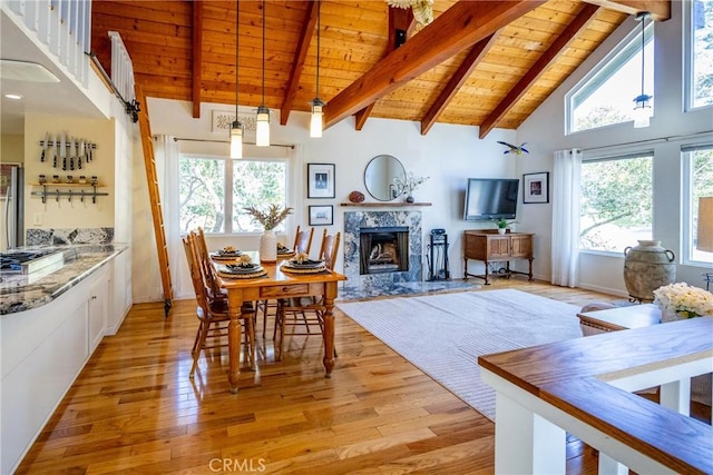 dining room with high vaulted ceiling, a high end fireplace, light hardwood / wood-style floors, wooden ceiling, and beamed ceiling