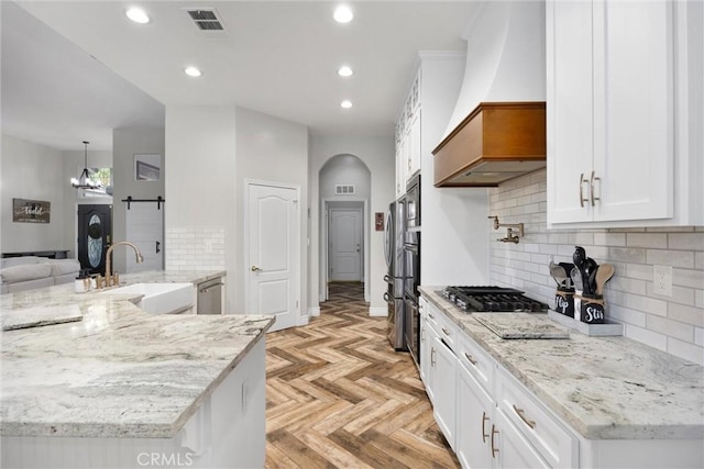 kitchen with sink, white cabinetry, custom range hood, light stone countertops, and light parquet floors