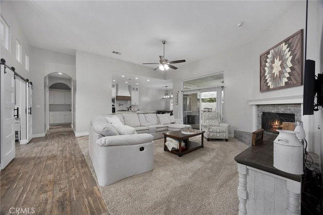 living room with ceiling fan, a fireplace, a barn door, and hardwood / wood-style floors