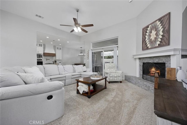 living room featuring a brick fireplace, light colored carpet, and ceiling fan