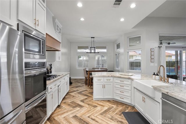 kitchen featuring sink, appliances with stainless steel finishes, white cabinets, decorative light fixtures, and light parquet flooring