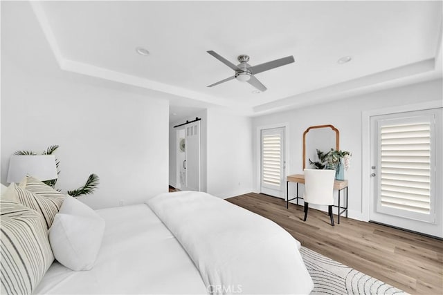 bedroom with a tray ceiling, ceiling fan, light hardwood / wood-style floors, and a barn door