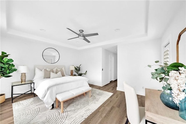 bedroom with wood-type flooring, ceiling fan, and a tray ceiling