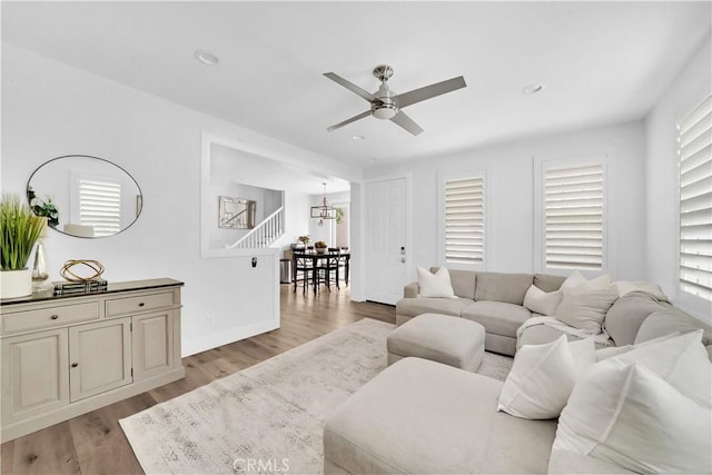 living room featuring ceiling fan with notable chandelier, light wood-type flooring, and plenty of natural light