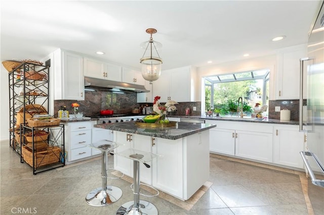 kitchen with white cabinetry, a center island, a kitchen bar, and dark stone counters