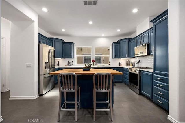 kitchen with butcher block countertops, appliances with stainless steel finishes, a kitchen island, blue cabinets, and decorative backsplash