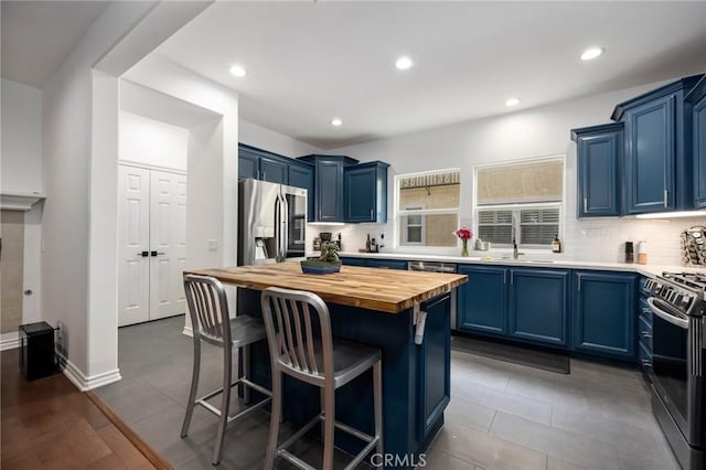 kitchen with butcher block countertops, blue cabinetry, appliances with stainless steel finishes, a center island, and decorative backsplash