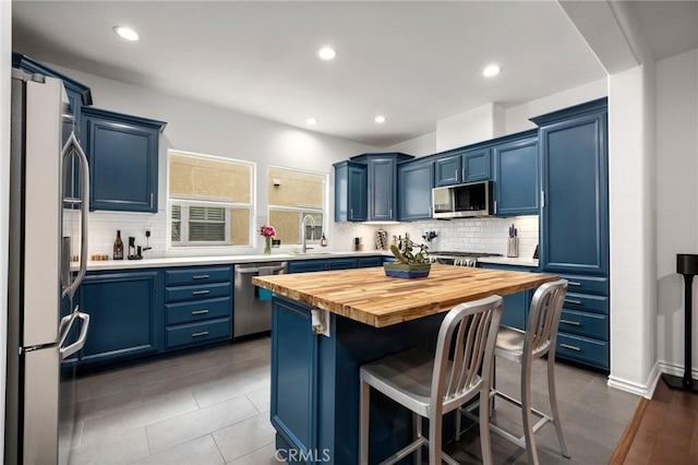 kitchen featuring blue cabinetry, wooden counters, appliances with stainless steel finishes, a kitchen island, and a kitchen bar