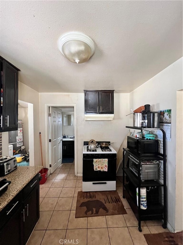 kitchen with white range with gas cooktop, light tile patterned floors, light stone counters, and a textured ceiling