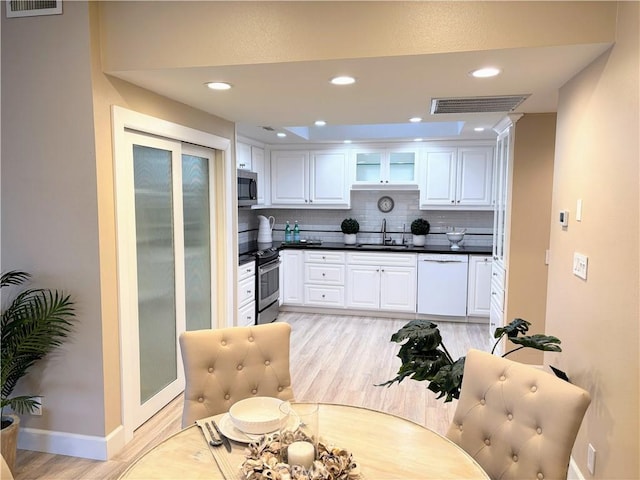 kitchen featuring sink, backsplash, stainless steel appliances, white cabinets, and light wood-type flooring