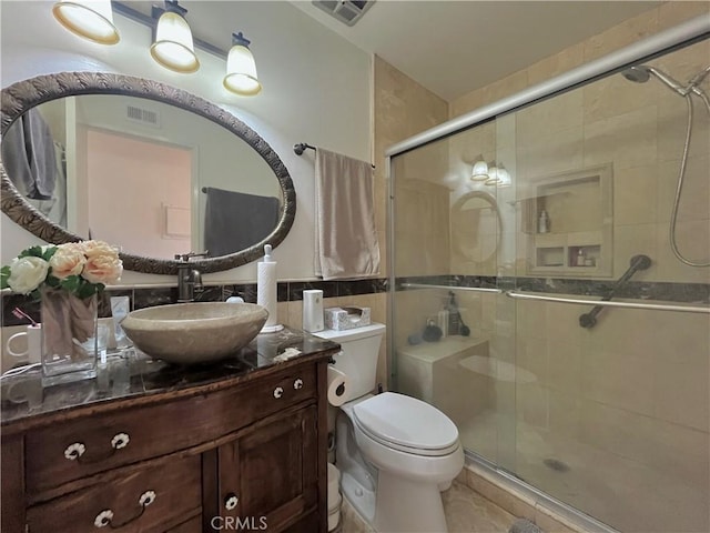 bathroom with vanity, toilet, a shower with door, and tile walls