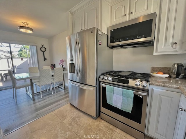 kitchen featuring white cabinetry, appliances with stainless steel finishes, light tile patterned flooring, and light stone counters