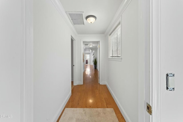 hall featuring light wood finished floors, baseboards, visible vents, and ornamental molding