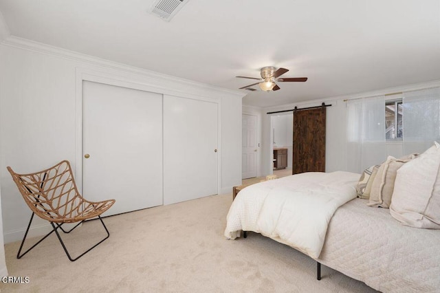 bedroom featuring a barn door, light carpet, visible vents, ornamental molding, and a closet