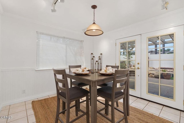 dining space with a wainscoted wall, light tile patterned flooring, ornamental molding, and french doors