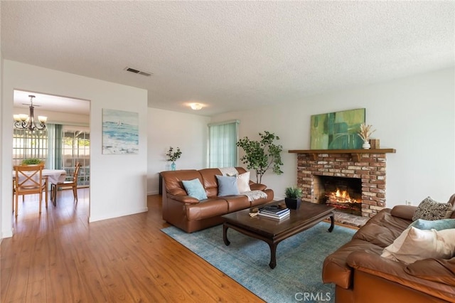 living room with a brick fireplace, hardwood / wood-style flooring, a textured ceiling, and a chandelier