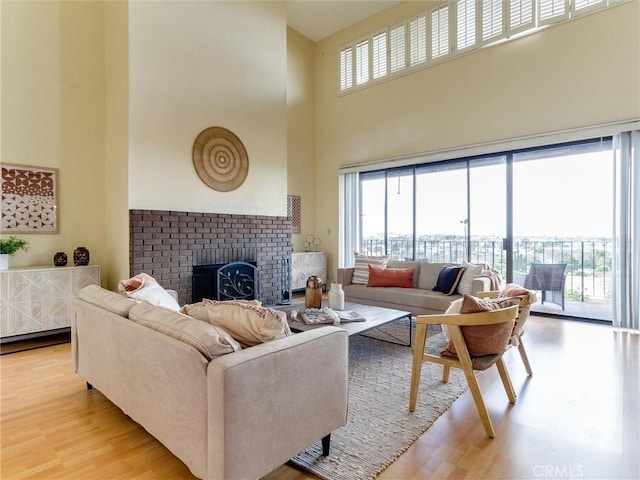 living room featuring a high ceiling, plenty of natural light, a fireplace, and light hardwood / wood-style flooring