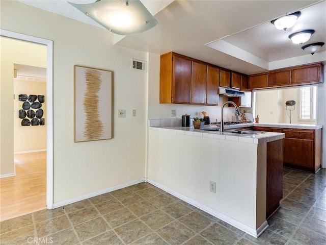 1923 Molino Ave Unit 303, Signal Hill, CA 90755 - kitchen featuring a peninsula, tile countertops, under cabinet range hood, baseboards, and a raised ceiling