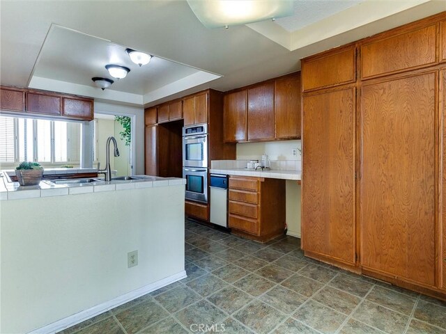 1923 Molino Ave Unit 303, Signal Hill, CA 90755 - kitchen with a raised ceiling, stainless steel double oven, brown cabinetry, a sink, and tile counters