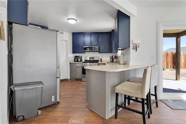 kitchen with blue cabinetry, appliances with stainless steel finishes, hardwood / wood-style floors, a kitchen breakfast bar, and kitchen peninsula