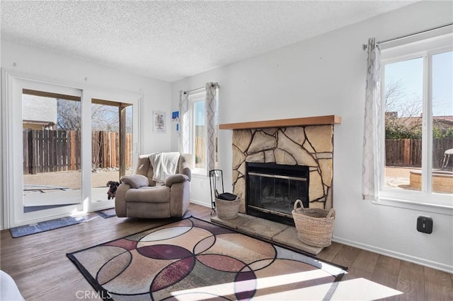 living room featuring a stone fireplace, wood-type flooring, and a textured ceiling