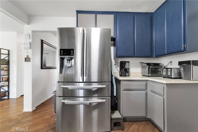 kitchen featuring stainless steel refrigerator with ice dispenser, dark hardwood / wood-style floors, blue cabinetry, and a textured ceiling