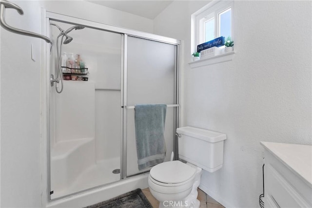 bathroom with a shower with door, vanity, tile patterned floors, and toilet