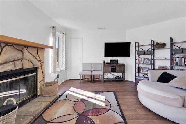 living room featuring a stone fireplace, dark wood-type flooring, and a textured ceiling