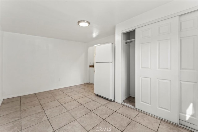 unfurnished bedroom featuring white refrigerator, a closet, and light tile patterned floors