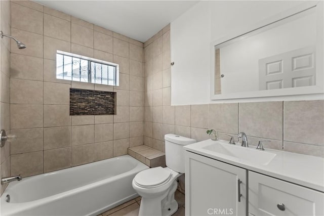 full bathroom with tile walls, decorative backsplash, tiled shower / bath combo, vanity, and toilet