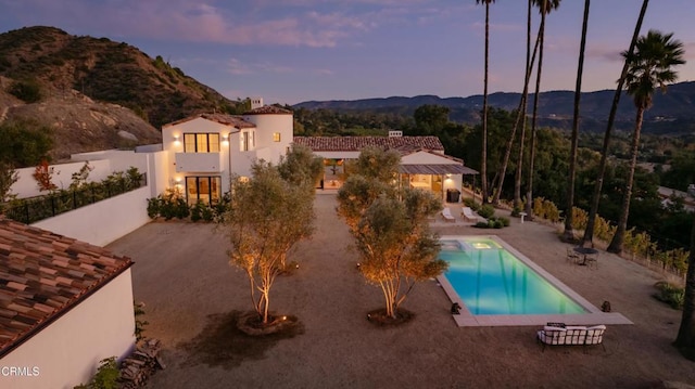 pool at dusk featuring a mountain view and a patio area
