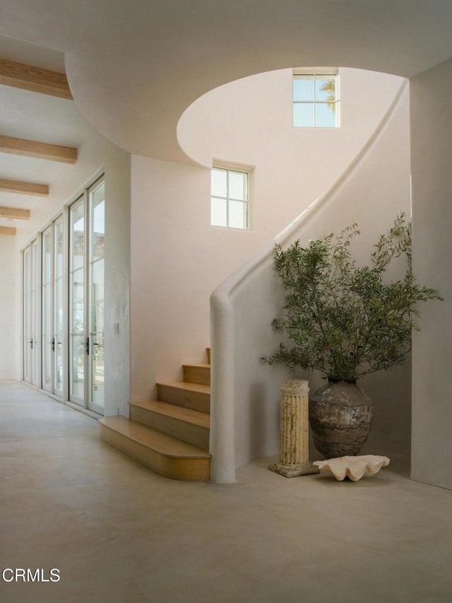 staircase with concrete flooring, a towering ceiling, and beam ceiling