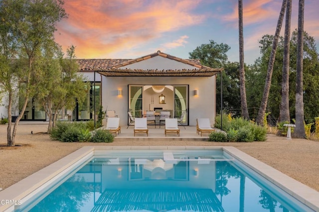 back house at dusk featuring a patio and an outdoor structure