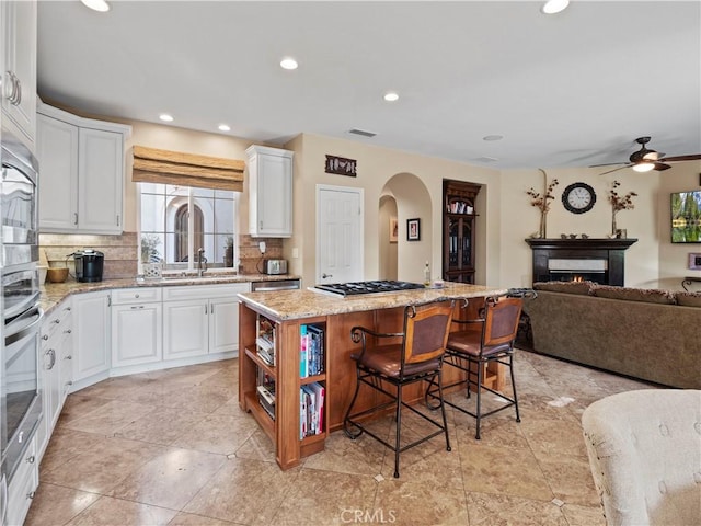 kitchen with white cabinetry, a kitchen island, a breakfast bar area, and light stone counters