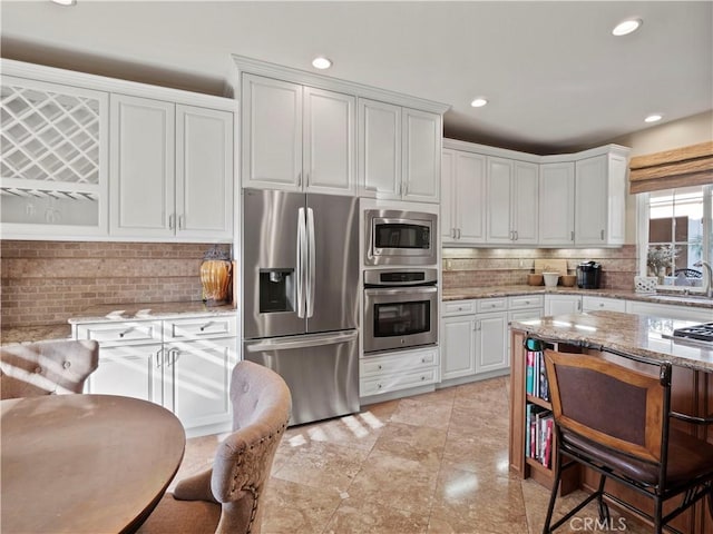 kitchen featuring white cabinetry, stainless steel appliances, light stone countertops, and backsplash