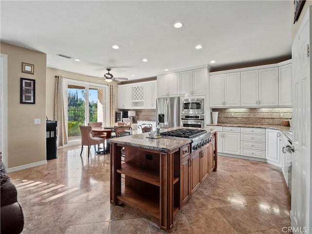 kitchen featuring white cabinetry, a center island, stainless steel appliances, light stone countertops, and decorative backsplash