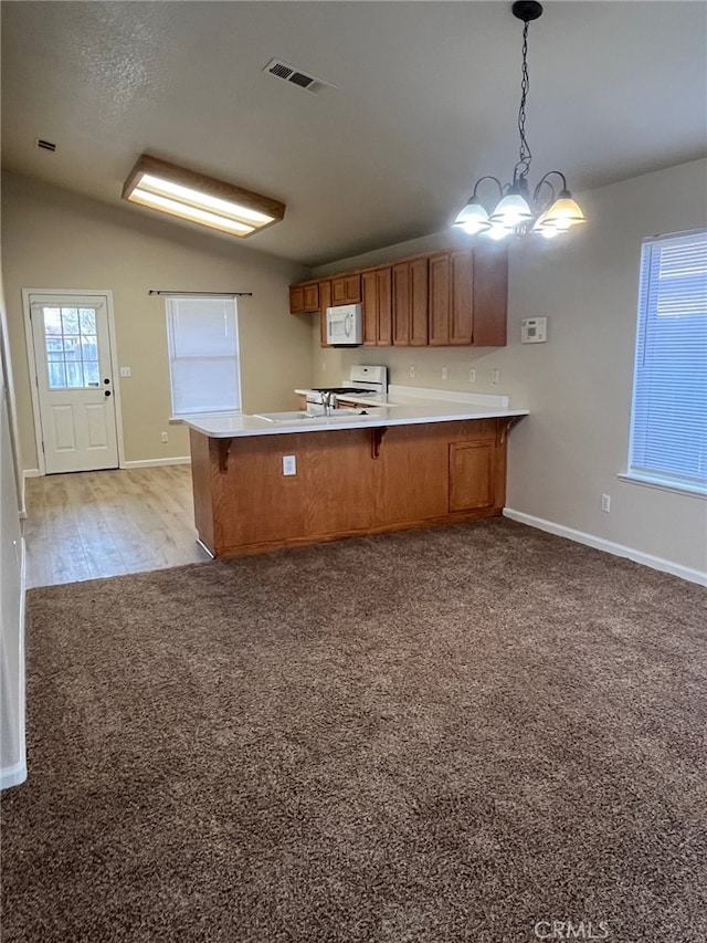 kitchen with lofted ceiling, white appliances, hanging light fixtures, light colored carpet, and kitchen peninsula