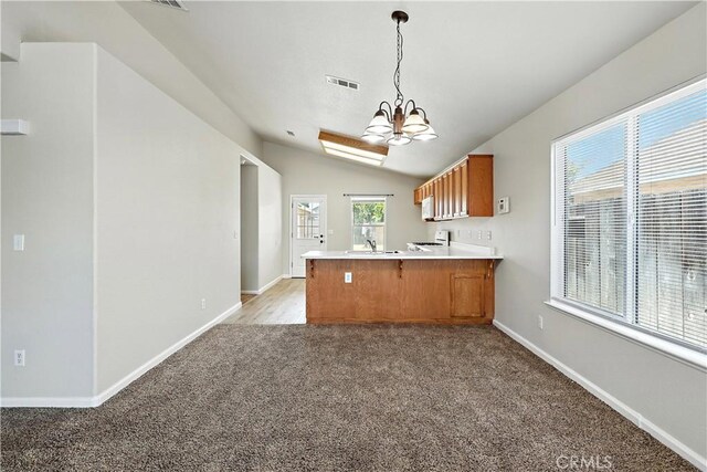713 Vista Del Rey Dr, Atwater, CA 95301 - kitchen with brown cabinetry, a peninsula, a chandelier, light colored carpet, and lofted ceiling