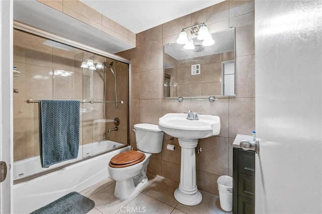 bathroom featuring tile walls, bath / shower combo with glass door, tile patterned floors, and toilet