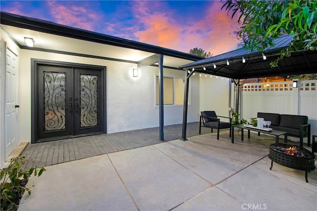 patio terrace at dusk with french doors, an outdoor living space with a fire pit, fence, and a gazebo