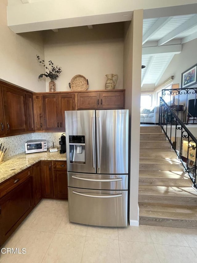 kitchen featuring light tile patterned floors, tasteful backsplash, light stone counters, stainless steel refrigerator with ice dispenser, and beam ceiling