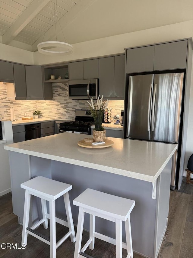 kitchen with lofted ceiling with beams, appliances with stainless steel finishes, a breakfast bar area, gray cabinets, and light countertops